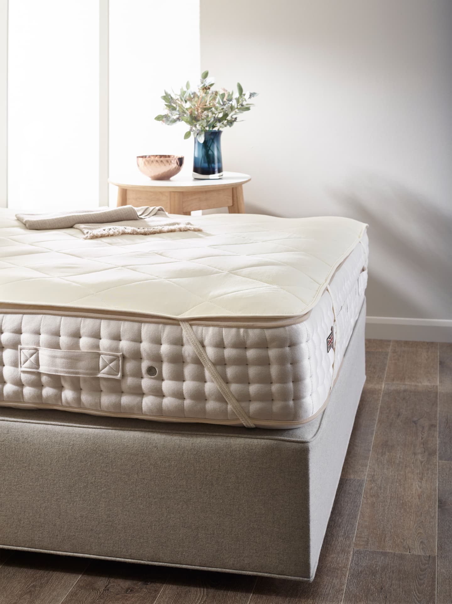 A quilted Vispring mattress protector fitted over a mattress in a light bedroom