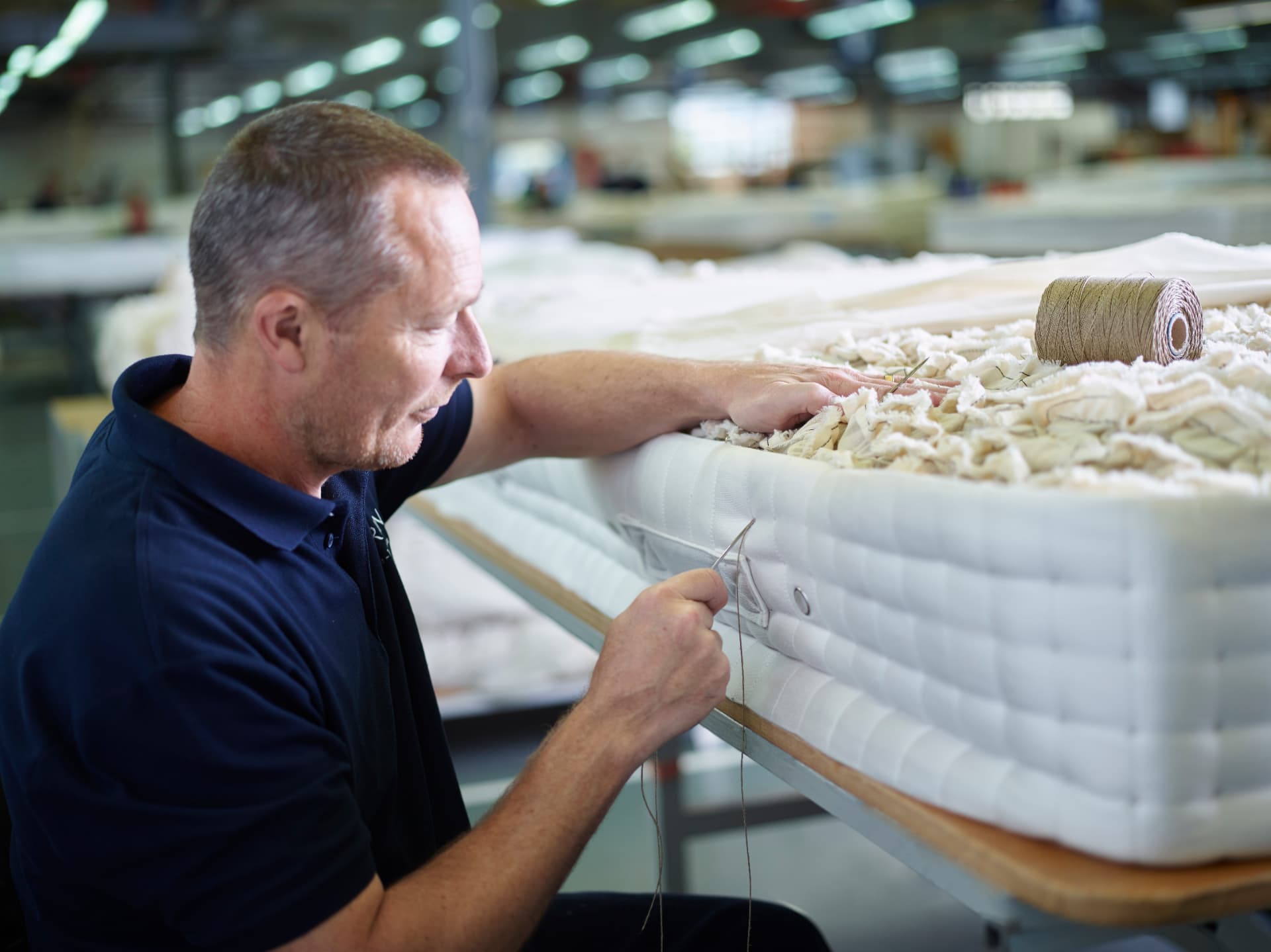 A craftsman hand-stitching the quilted side border of a white Vispring mattress with a long needle