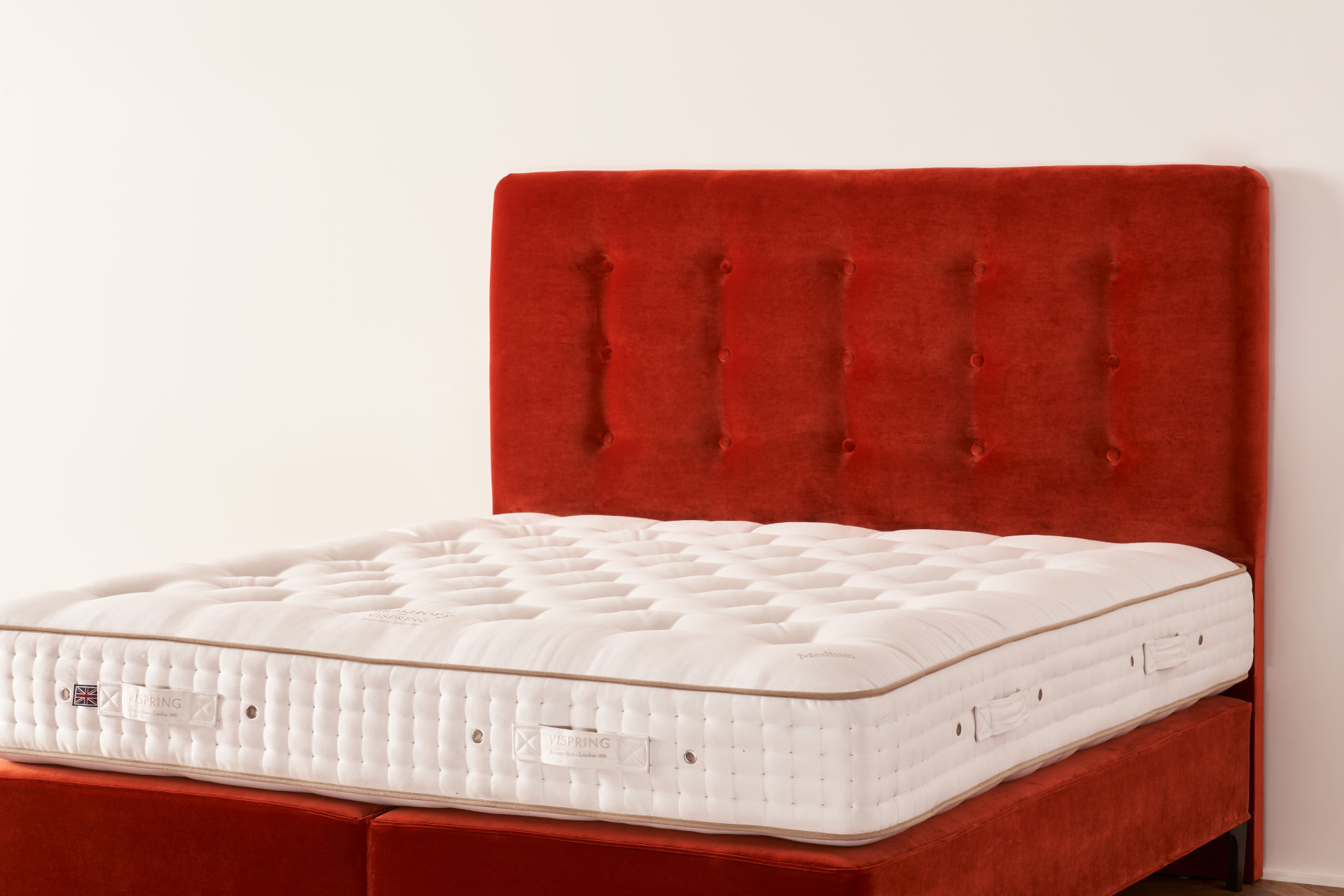 The Achilles headboard, a deep buttoned design in burnt-orange velvet on a Vispring bed