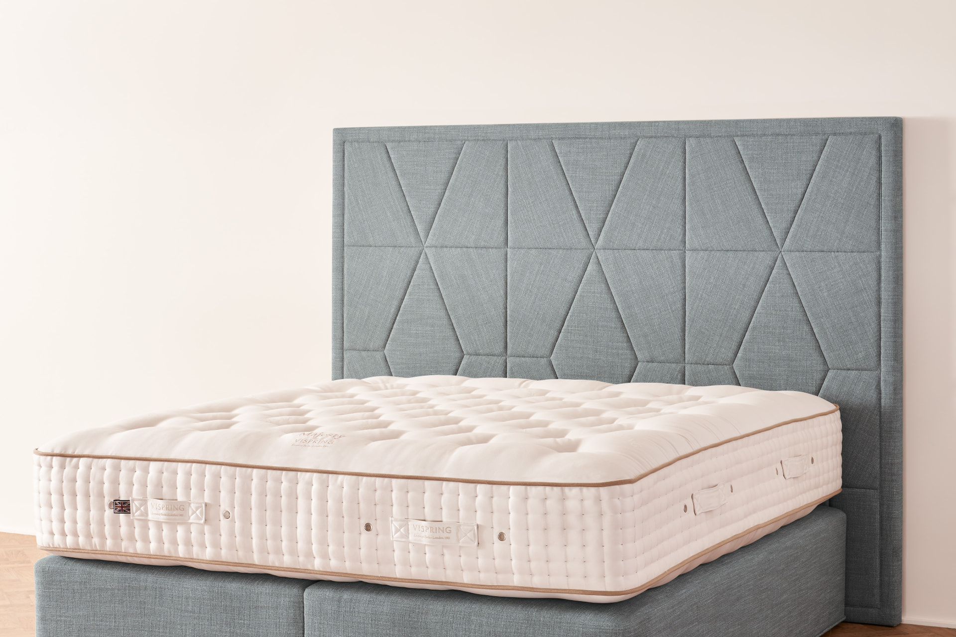 The Berkeley headboard, a geometric panel of folded facets in blue-grey fabric on a Vispring bed