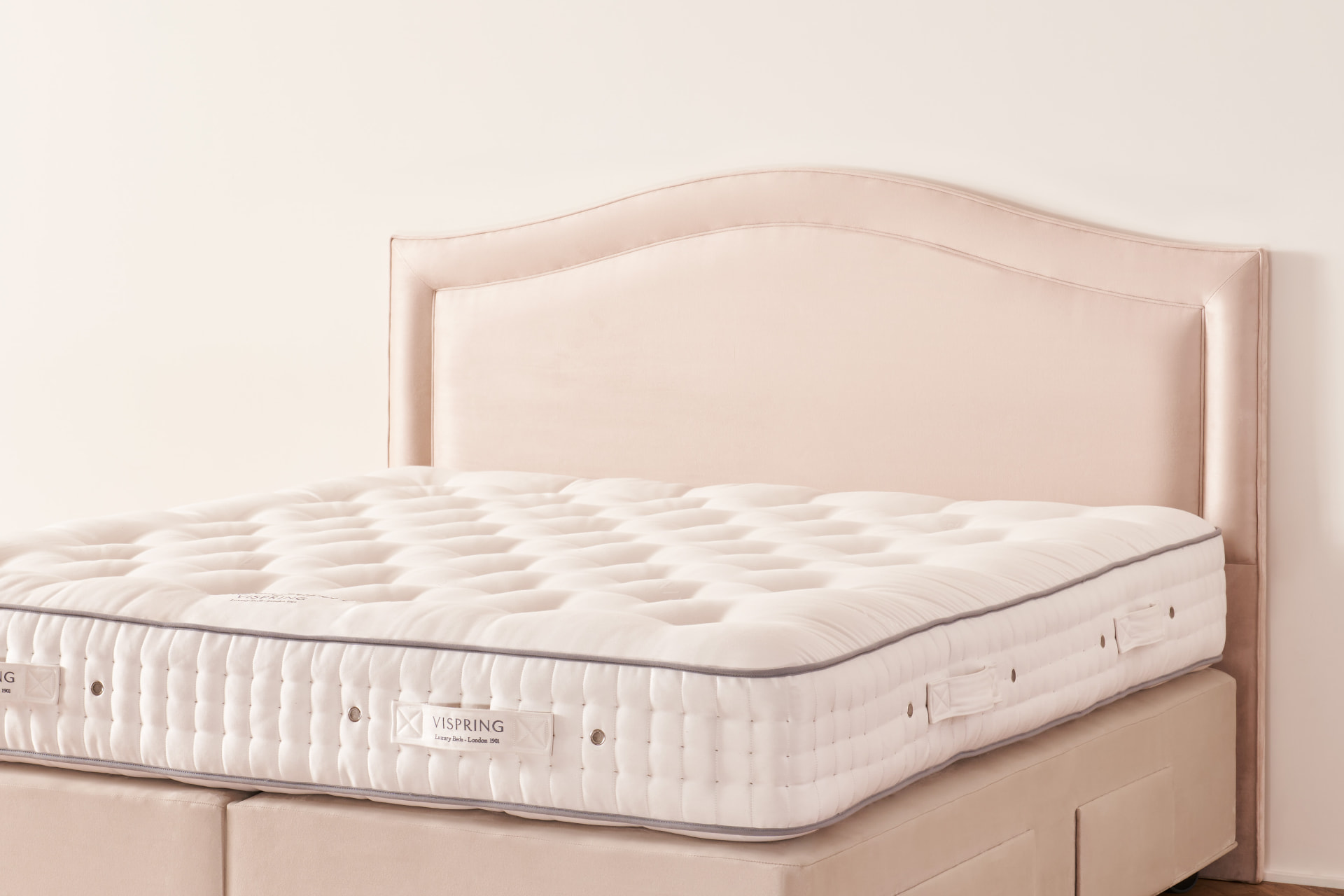 The Artemis headboard, a softly arched panel in pale blush fabric on a Vispring bed