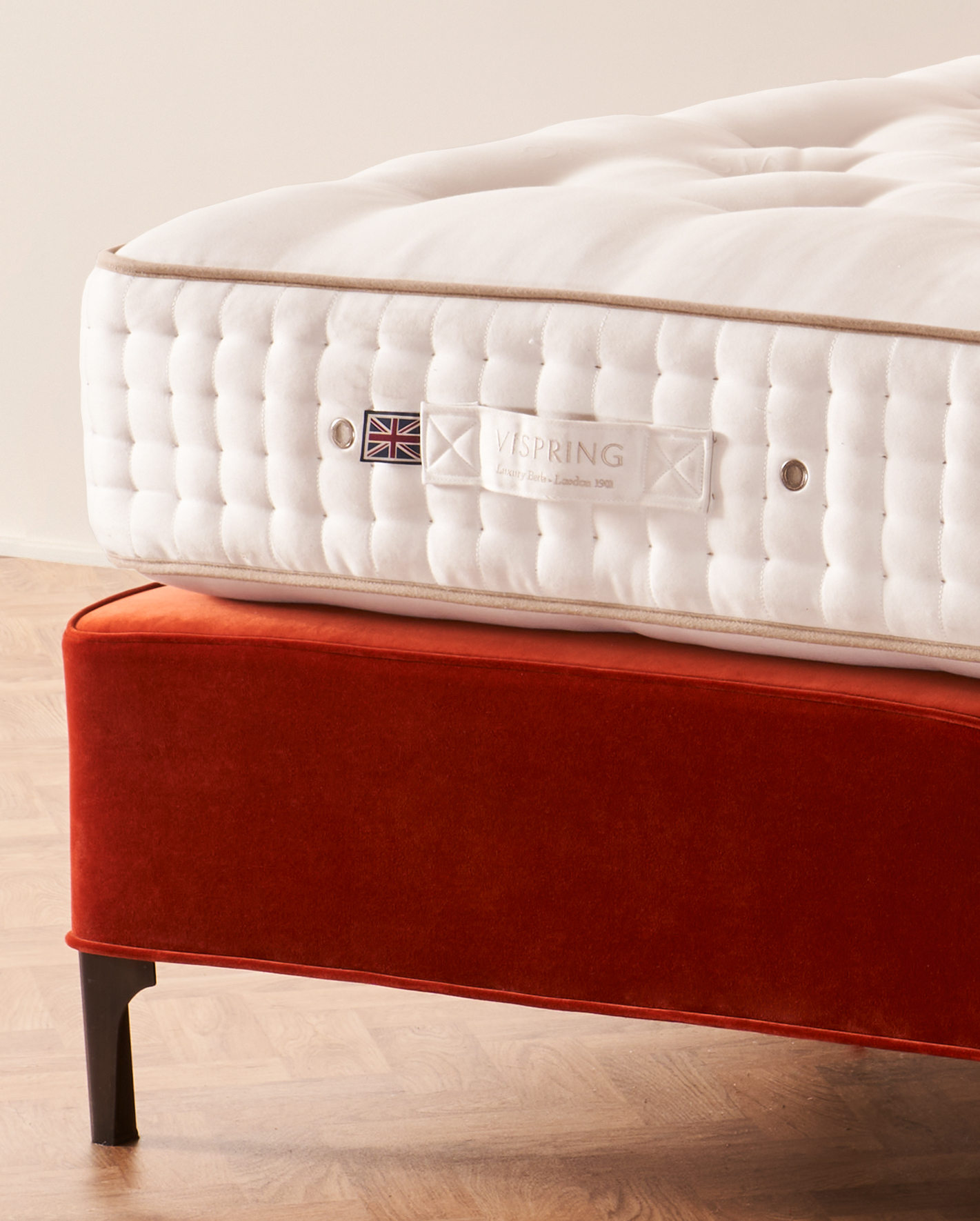 The Vispring Signatory mattress, hand side-stitched in ivory, on a burnt-orange velvet divan