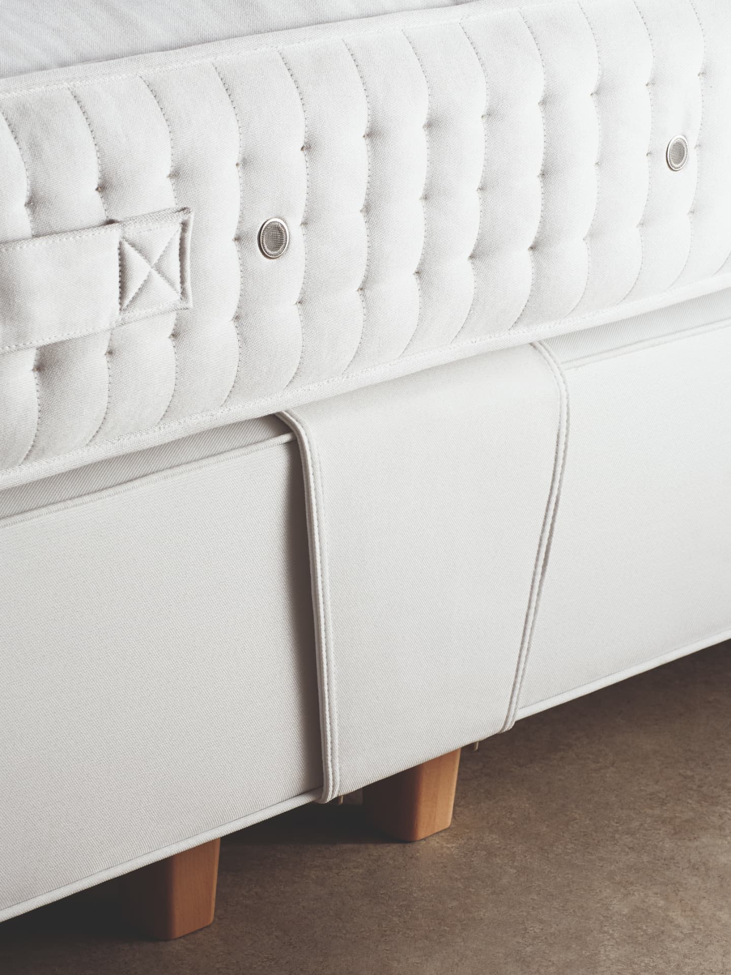 Close detail of a white fabric mantle folding over the corner of a Vispring divan on timber legs