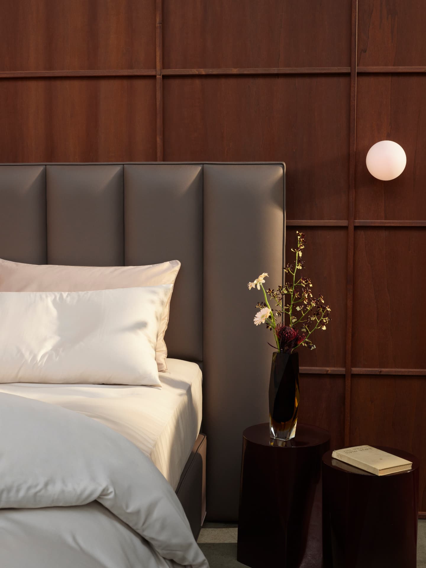 Detail of a channelled grey leather headboard beside a sculptural side table
