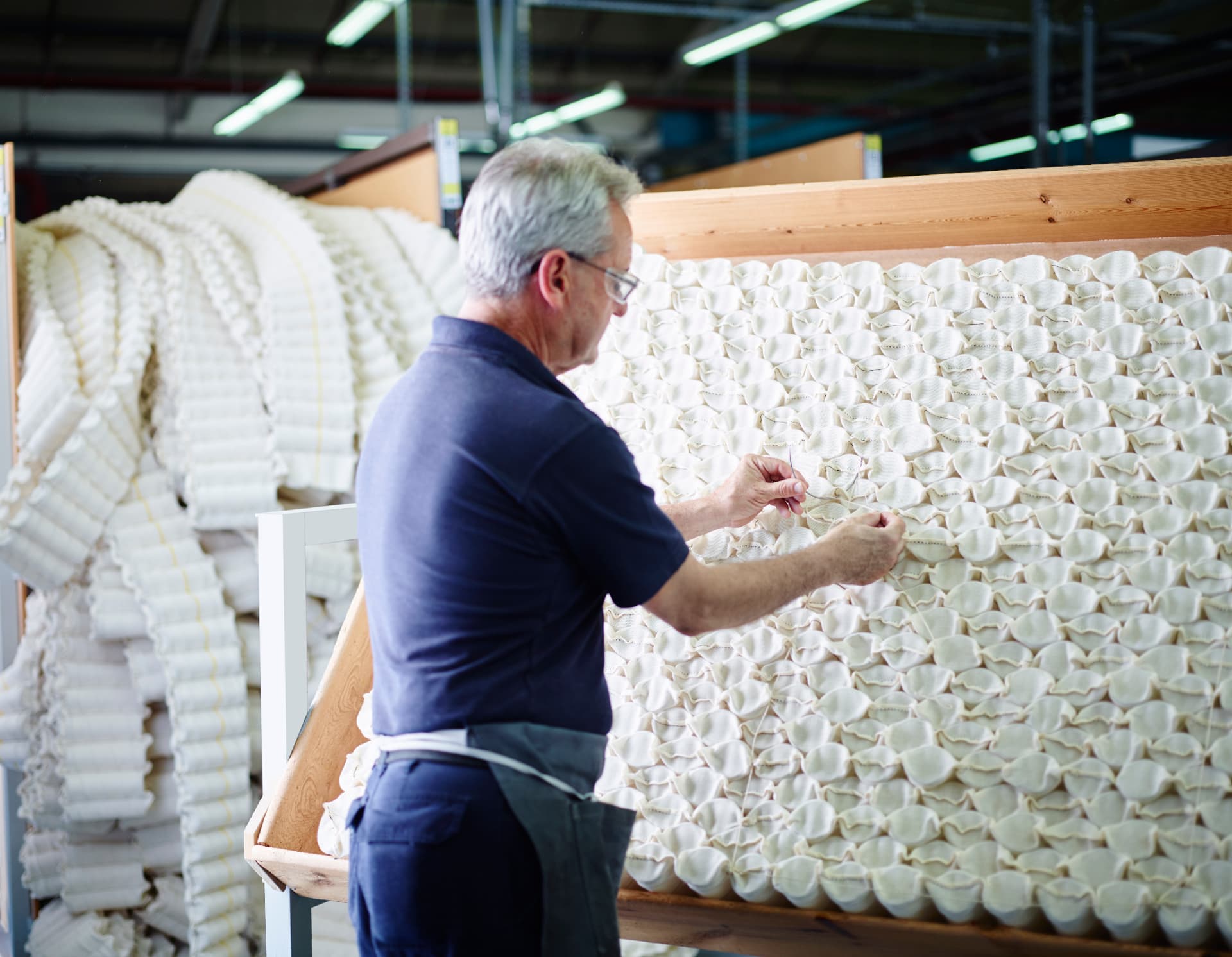 A craftsman hand-nesting individual pocket springs into a grid within a wooden frame