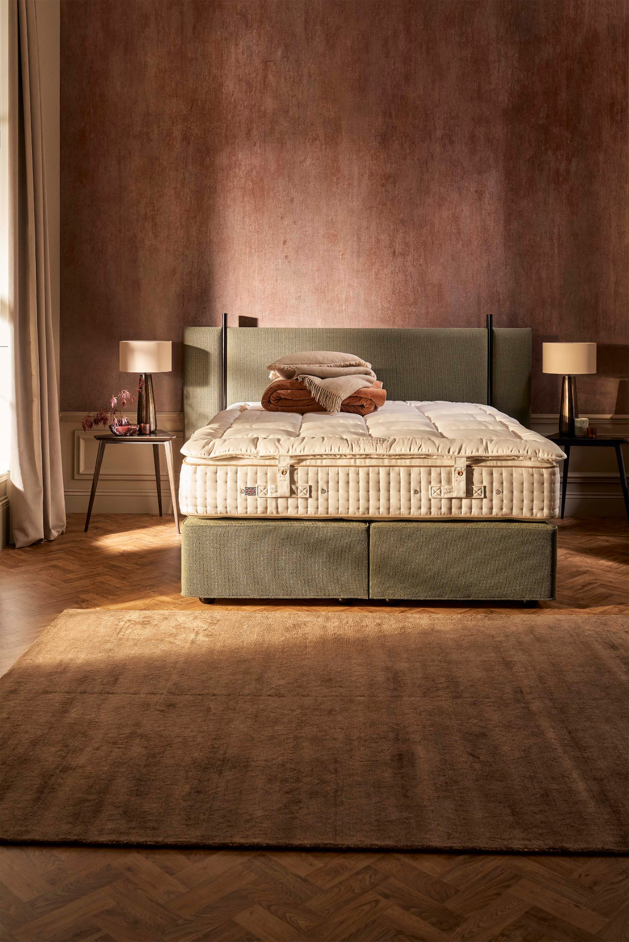 The Opulence topper on a Vispring bed in a copper-toned room, with folded blankets resting on top