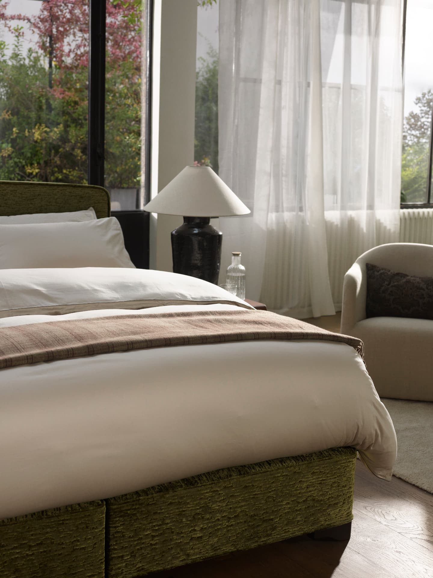 Olive upholstered divan dressed with soft bedlinen and a woven throw