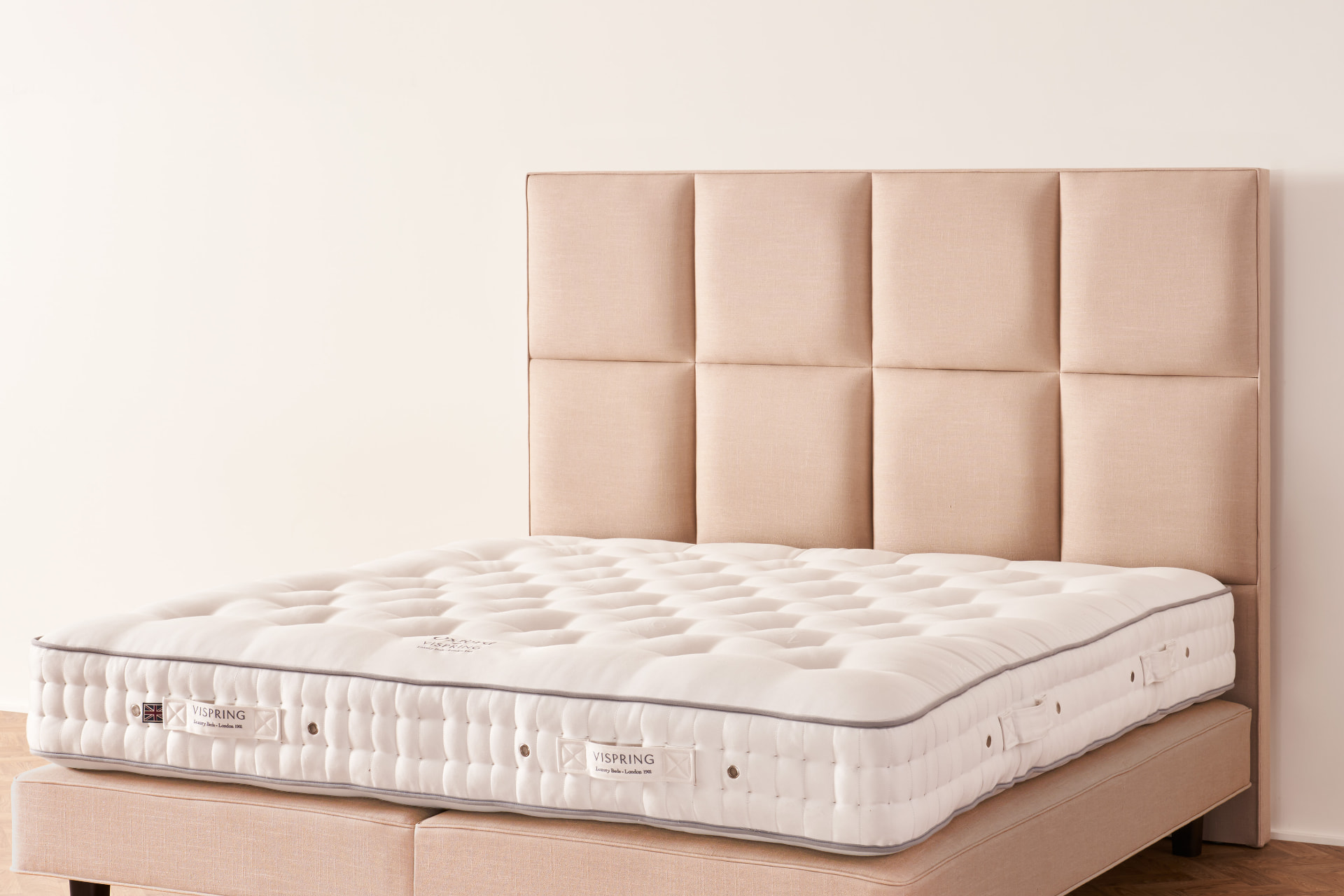 The Atlas headboard, a grid of generously padded squares in warm sand linen on a Vispring bed