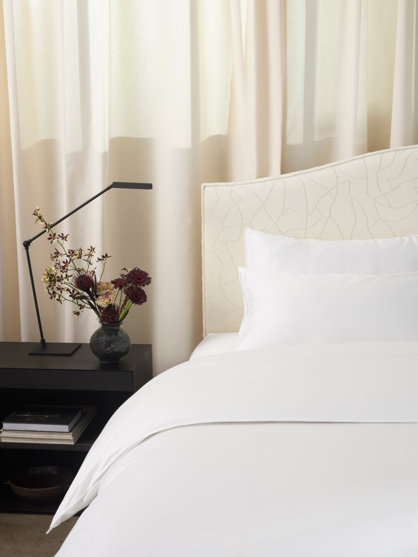 Ivory quilted headboard and crisp white bedlinen beside a dark bedside table