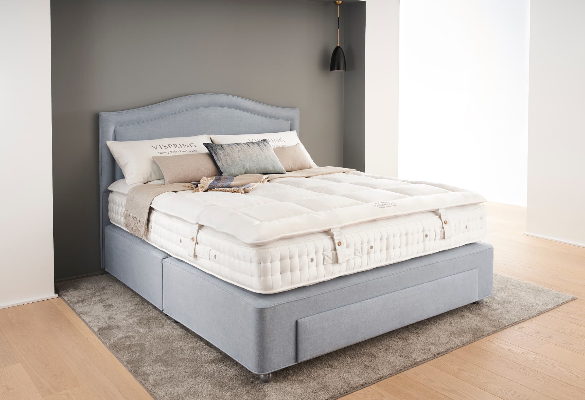 A Vispring bed finished with a Pillowtop topper, dressed in white bedlinen against a grey wall